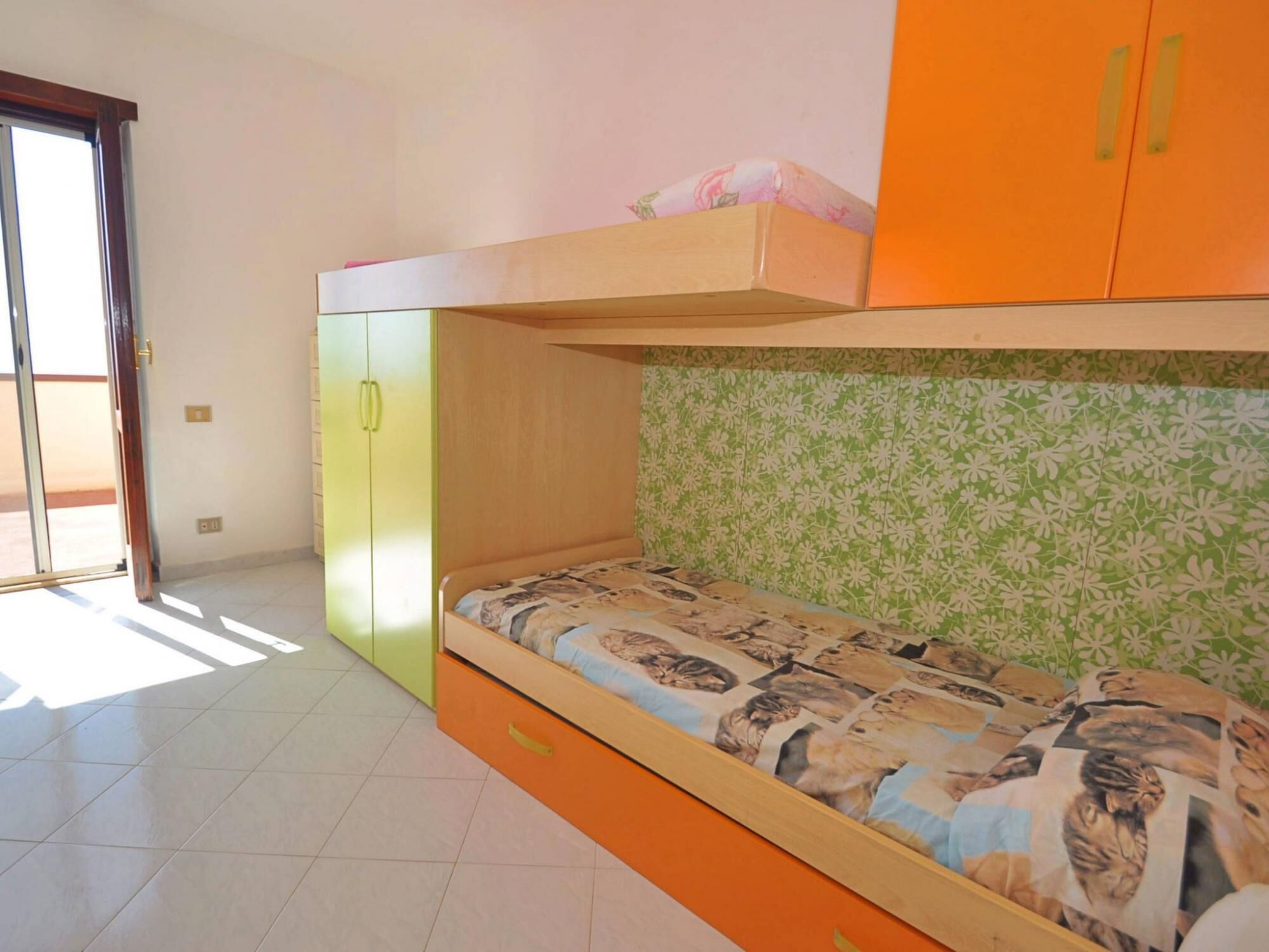 A bedroom with a bunk bed, a green patterned wall, and a sliding door.