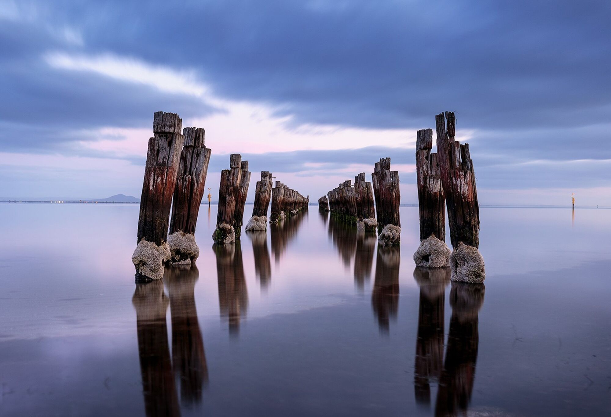 A calm lake with wooden posts in the center, surrounded by a clear sky.