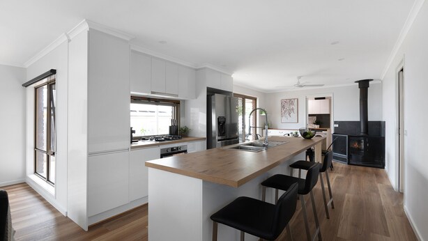 Una cocina moderna con armarios blancos, una isla de madera, taburetes negros y un estufa de leña.