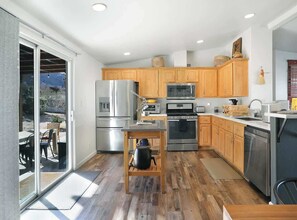 Une cuisine moderne avec des meubles en bois, des appareils en acier inoxydable et une porte-fenêtre coulissante donnant sur un espace extérieur.
