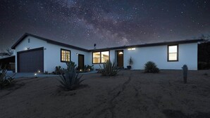 A modern house with a garage, multiple windows, and a desert garden at night. - JT Starry Night Getaway Pet-Friendly (Joshua Tree)