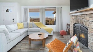 A modern living room with a sectional sofa, a round coffee table, a fireplace, and a large TV mounted on the wall. - JT Starry Night Getaway Pet-Friendly (Joshua Tree)