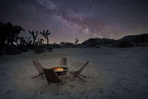 Eine Wüstenlandschaft bei Nacht mit Sternenhimmel, einem Lagerfeuer und drei Stühlen.
