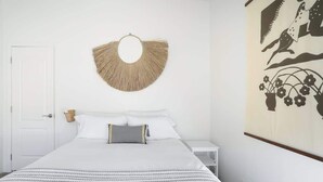 A bedroom with a bed, a bedside table, a wall-mounted decorative item, and a wall painting. - JT Starry Night Getaway Pet-Friendly (Joshua Tree)
