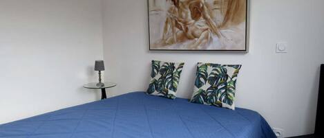 Een slaapkamer met een groot bed, een schilderij aan de muur en een kleine tafel met een lamp.