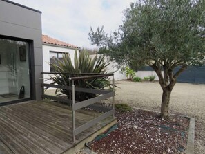 A modern building with a wooden deck, a metal railing, and a tree in the foreground. - Maison Chaleureuse Cité en Centre Ville a 15 Minute de la Plage (Jard-sur-Mer)
