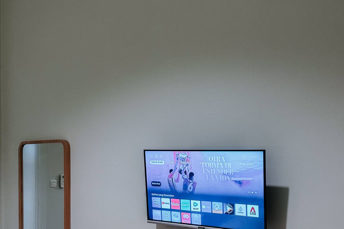 Un televisor de pantalla plana montado en una pared sobre un estante de madera, con un espejo a la izquierda.