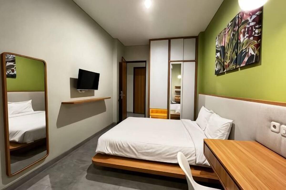 Habitación de hotel con una cama, televisión, espejo, mesita de madera y pared verde.