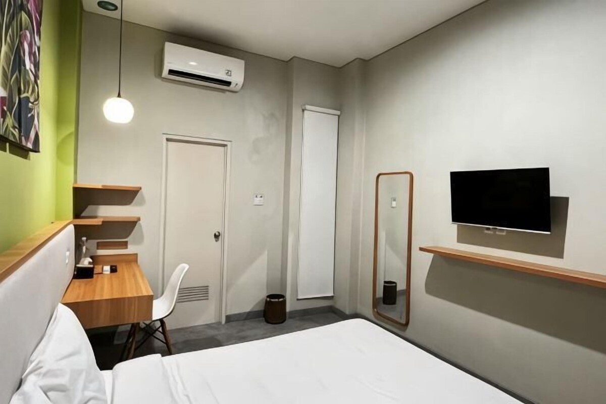 Una habitació d'hotel amb un llit, una taula de treball amb una cadira, un televisor fixat a la paret i un aparell d'aire condicionat.