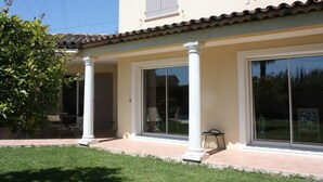 Una casa de dos pisos con un porche cubierto, grandes puertas corredizas de vidrio y techo de tejas.