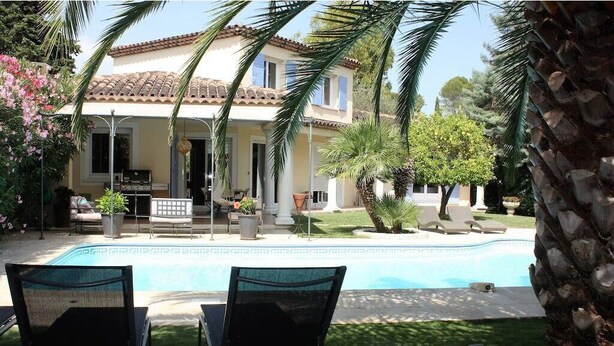 Una casa de dos pisos con piscina, mobiliario exterior y un jardín bien cuidado.