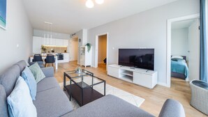 Ein modernes Wohnzimmer mit einem grauen Sofa, einem Glastisch und einem Flachbildfernseher auf einer weißen Ablagefläche.