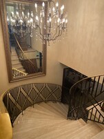 Una imponente escalera con candelabro y un gran espejo.
