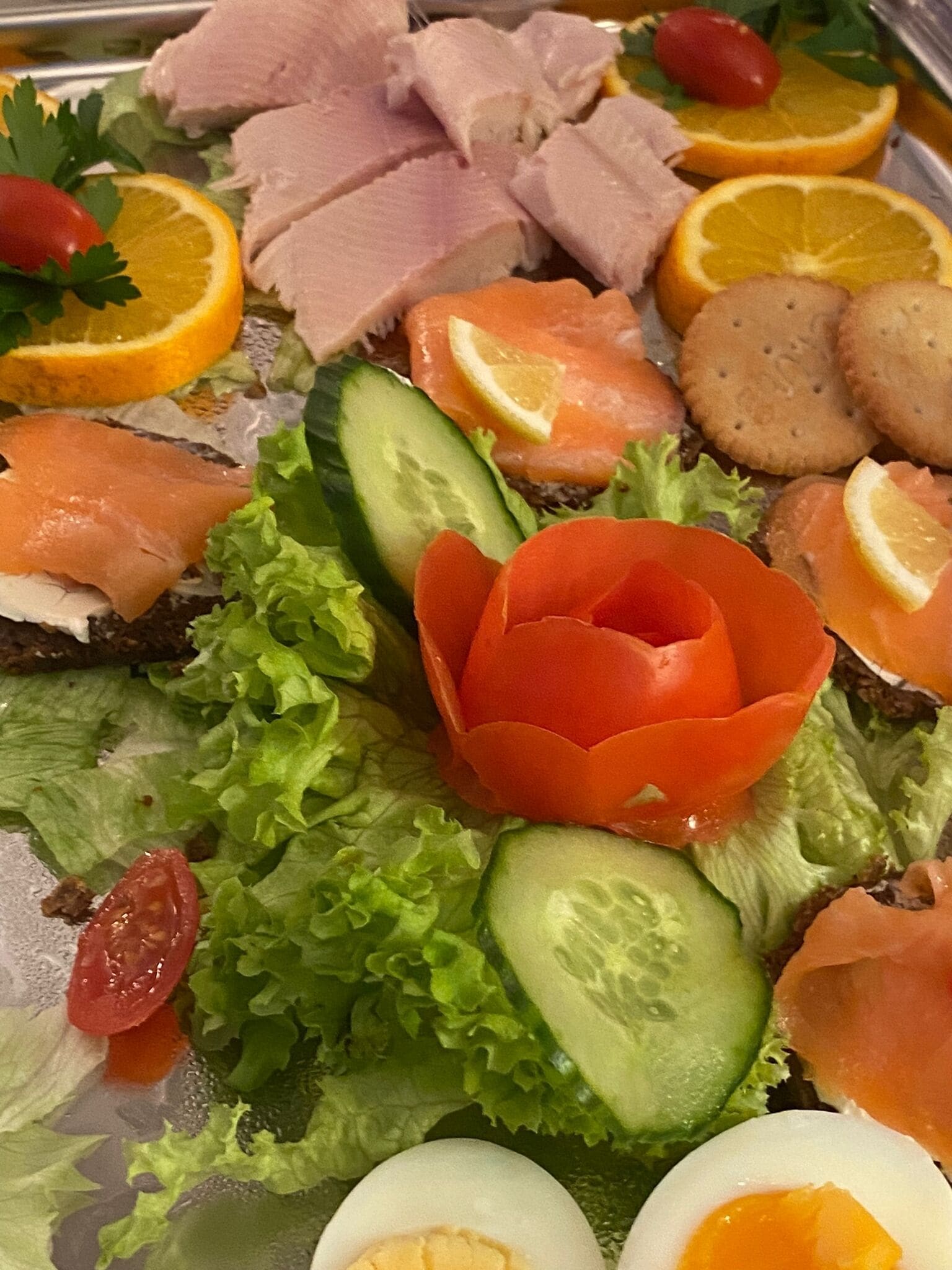 A platter of food including smoked salmon, eggs, cucumbers, and tomatoes.
