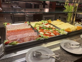 Un bufé con diversas opciones de comida, incluyendo carnes, quesos y verduras.