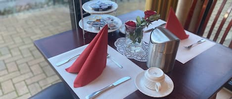 A table set with a white plate, a cup, a silver pitcher, and a glass vase with roses.