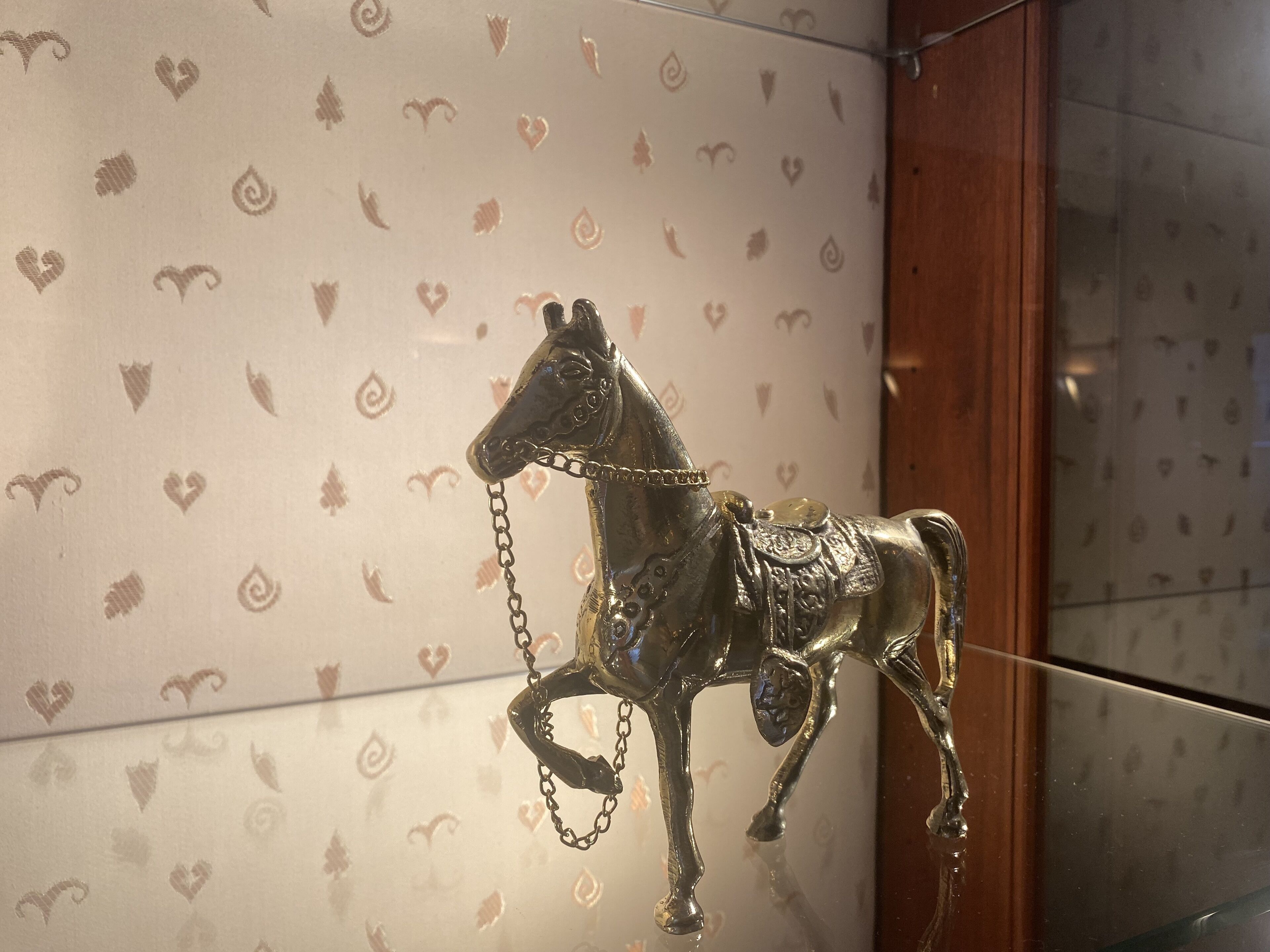 A decorative metal horse sculpture mounted on a wall with a heart-patterned wallpaper.