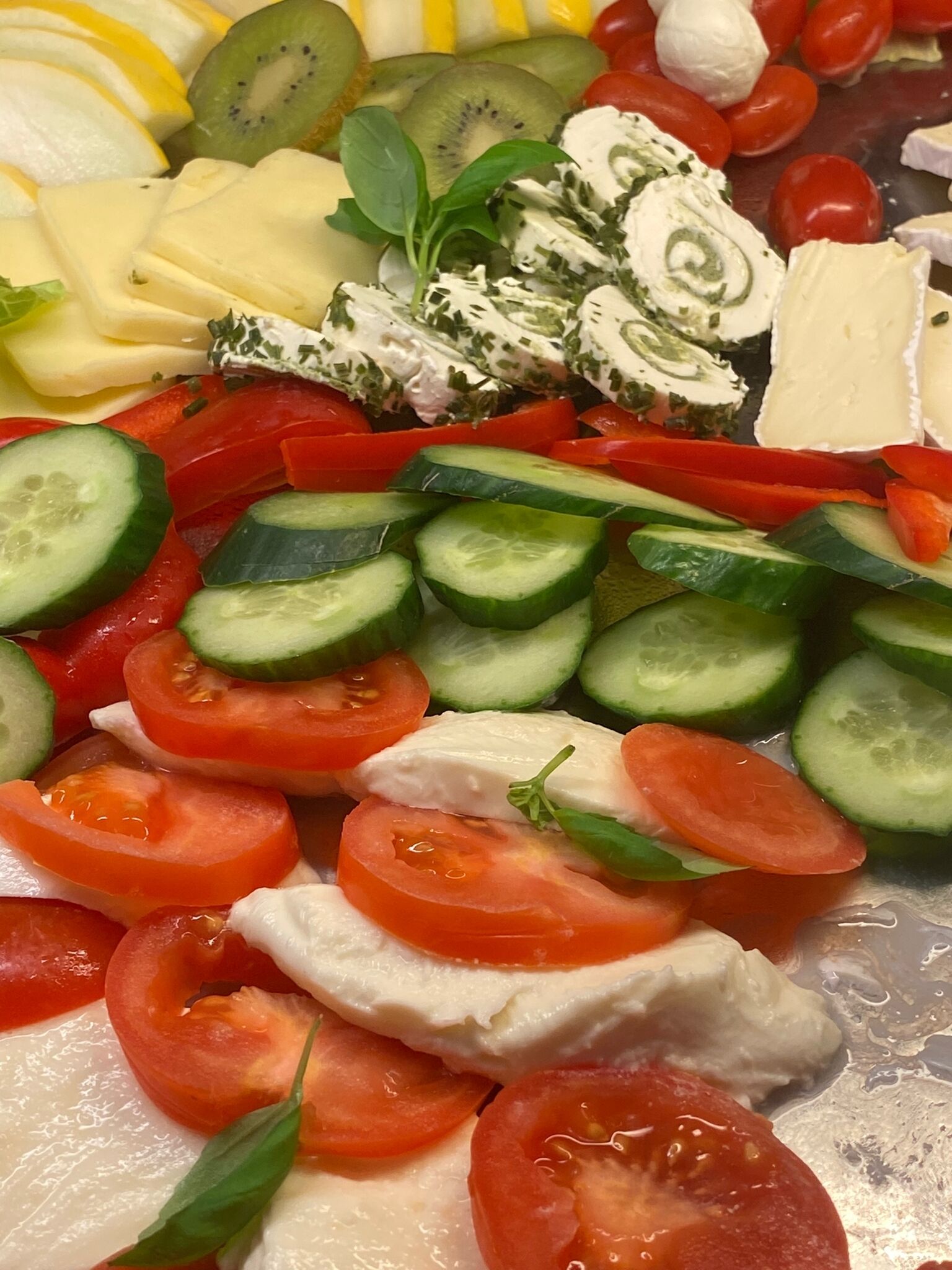 A variety of fresh fruits and vegetables, including tomatoes, cucumbers, and kiwi slices, arranged on a tray.