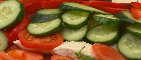 A variety of fresh fruits and vegetables, including tomatoes, cucumbers, and kiwi slices, arranged on a tray.