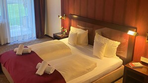 A hotel room with a large bed, a nightstand, a lamp, and a window with curtains. - Hotel Villa Sophia (Warendorf)