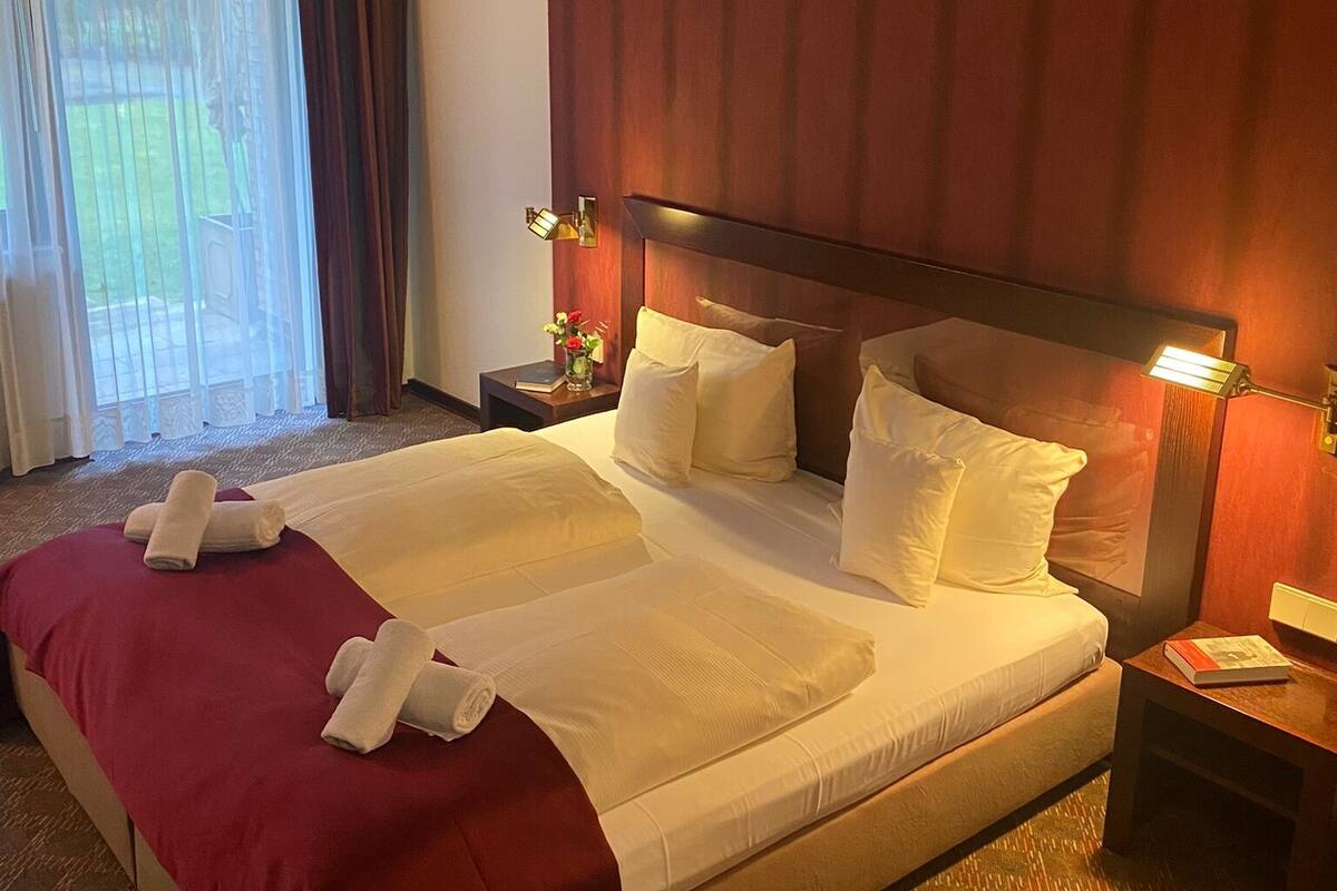 Une chambre d’hôtel avec un grand lit, une table de chevet, une lampe et une fenêtre avec des rideaux.