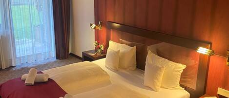 Habitación de hotel con una cama grande, una mesita de noche, una lámpara y una ventana con cortinas.