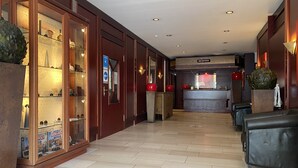 A hotel lobby with a reception desk, seating area, and a glass display case with board games. - Hotel Villa Sophia (Warendorf)