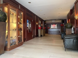 Un vestíbulo de hotel con mostrador de recepción, zona de estar y una vitrina de cristal con juegos de mesa.