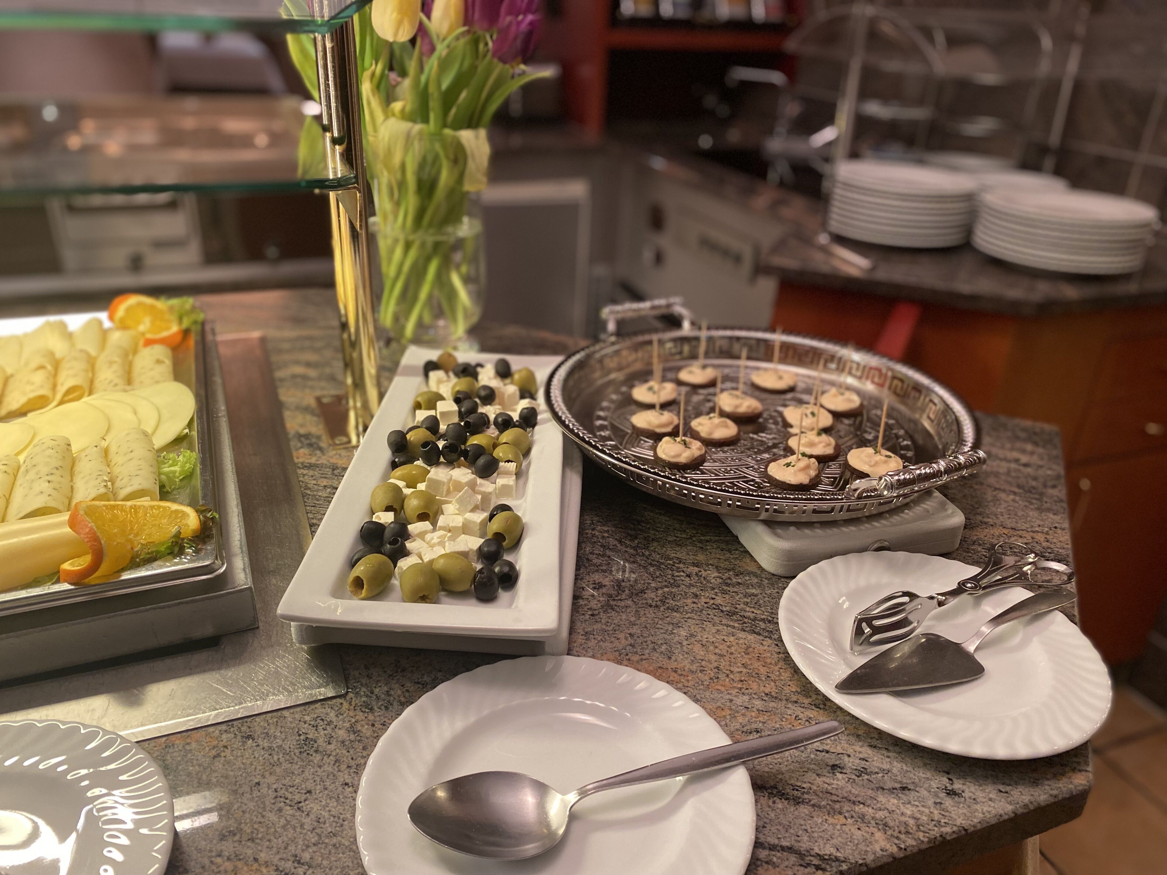 A buffet setup with various food items including cheese, olives, and bread rolls.