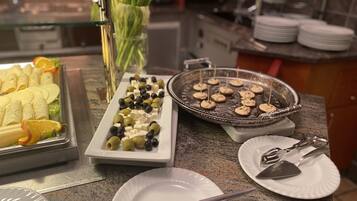 A buffet setup with various food items including cheese, olives, and bread rolls.
