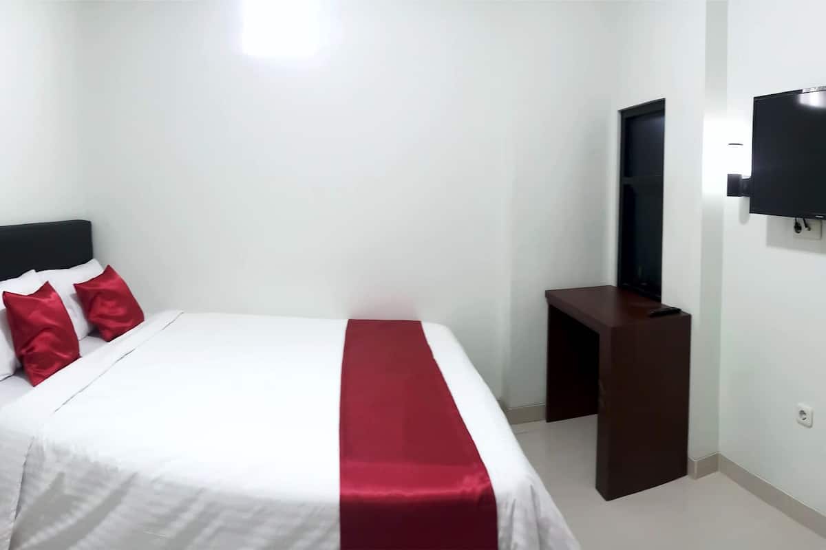 A hotel room with a bed, a TV mounted on the wall, a small wooden nightstand, and a wardrobe.