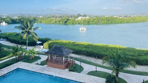 Un espace piscine agrémenté d’un kiosque, de palmiers et offrant une vue sur un lac où se trouve un bateau.
