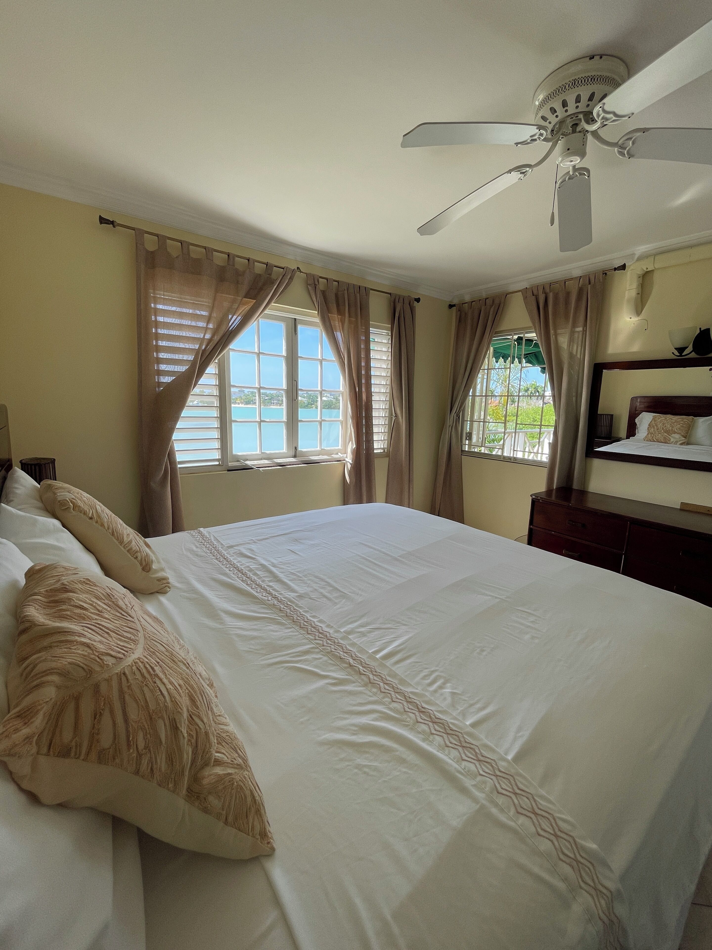 A hotel room with a large bed, a ceiling fan, a window with curtains, and a view of the outdoors.