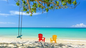 Une plage avec deux chaises colorées et une balançoire sous un arbre.