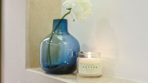 Un vase bleu contenant une fleur blanche et une bougie allumée, sur laquelle est apposée une étiquette indiquant le mot « Coton », est posé sur une étagère.