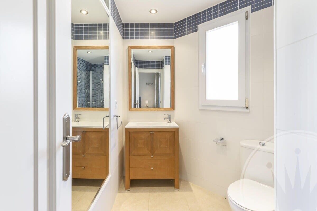 A bathroom with two sinks, wooden cabinets, a toilet, and a shower area.