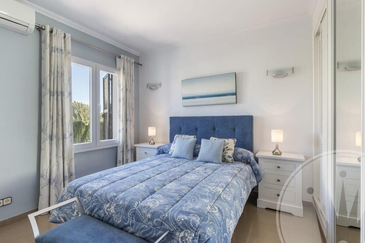 A bedroom with a large bed, two bedside tables, a headboard, and a window with curtains.