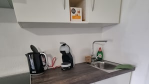 Eine kleine Küche mit Herd, Kaffeemaschine, Spüle und einem Schrank mit einer Flasche Geschirrspülmittel.