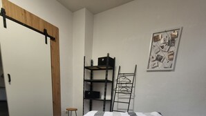 Ein Schlafzimmer mit einem Bett, einer Holztür, einem Metallregal und einem an der Wand hängenden Bild.