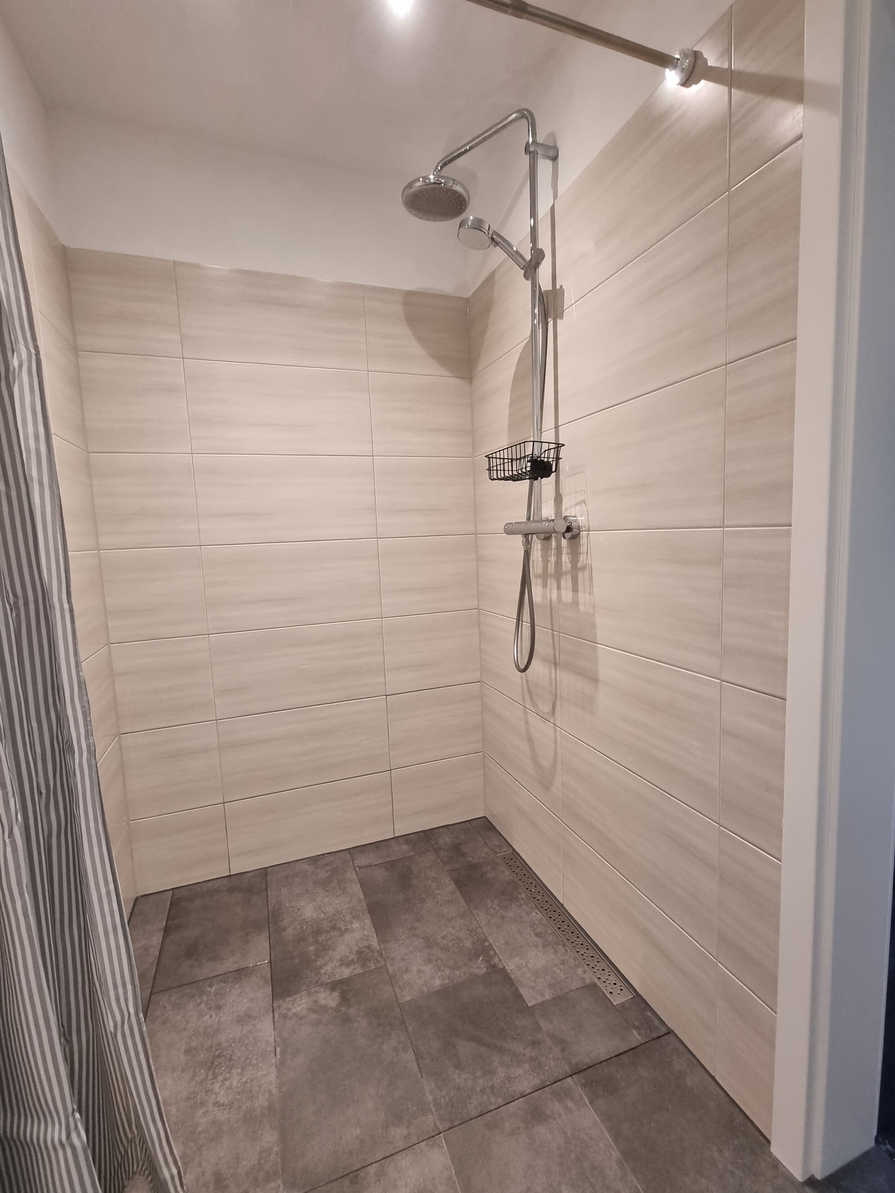 A modern shower with a handheld showerhead and a wall-mounted faucet, tiled walls, and a striped shower curtain.