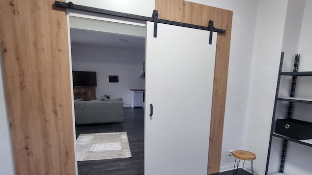 Ein modernes Interieur mit einer Schiebetür zu einem Wohnbereich, dunklem Holzboden und einem Metallregal.