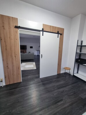 Un intérieur moderne avec une porte coulissante donnant sur un espace de vie, un parquet en bois foncé et une étagère en métal.