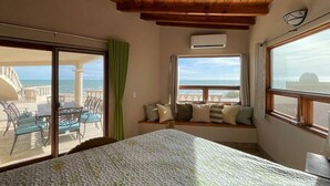 A bedroom with a large bed, a view of the sea, a window seat with cushions, and a wooden ceiling. - Casa Semana- Beachfront home (up to 16 guests!) (Playa La Jolla)