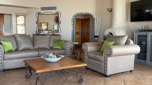A living room with a sofa, two armchairs, a coffee table, a mirror, a fireplace, and a television. - Casa Semana- Beachfront home (up to 16 guests!) (Playa La Jolla)