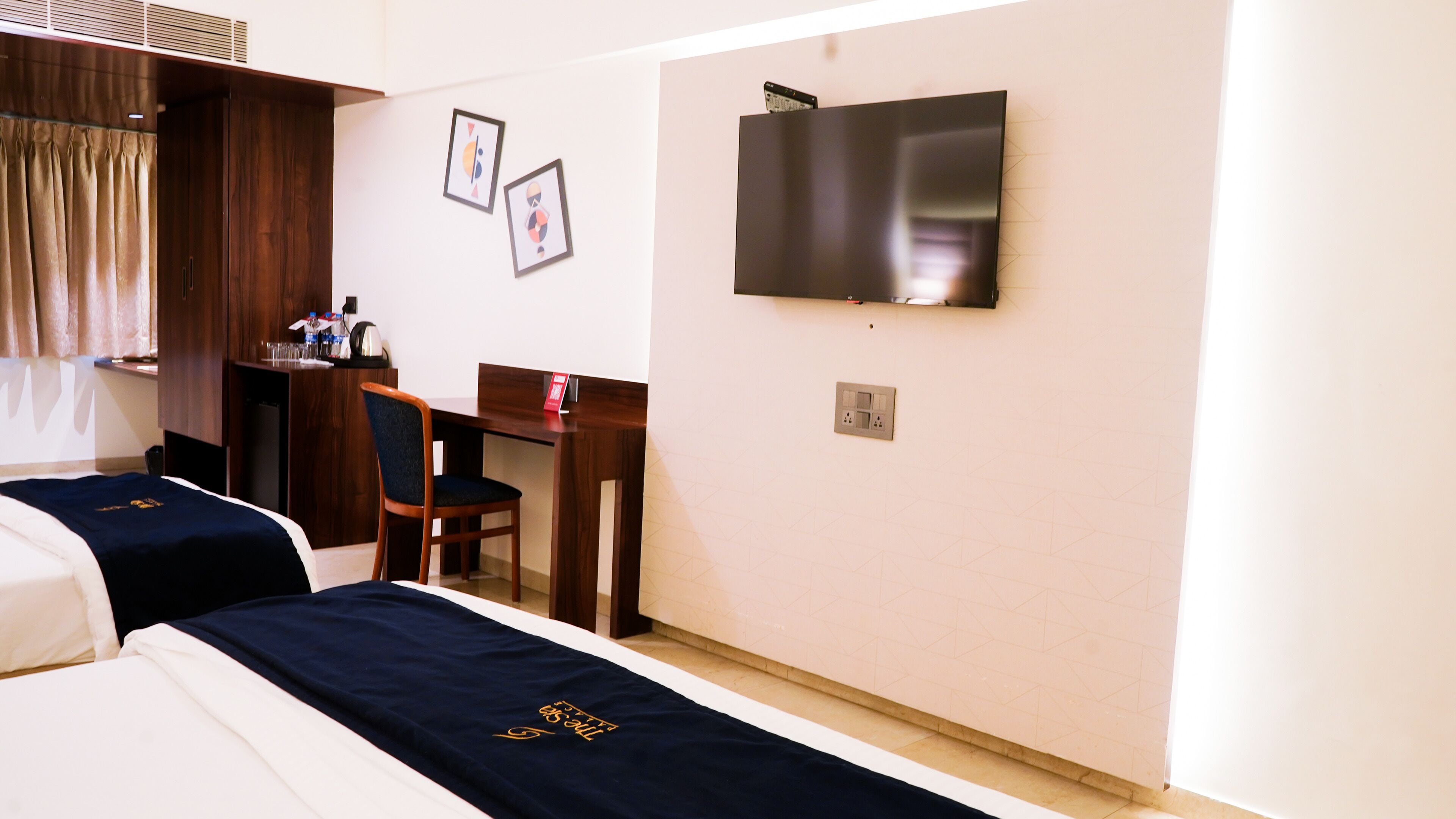 Ett hotellrum med två sängar, ett skrivbord, en stol, en tv och ett litet pentry.