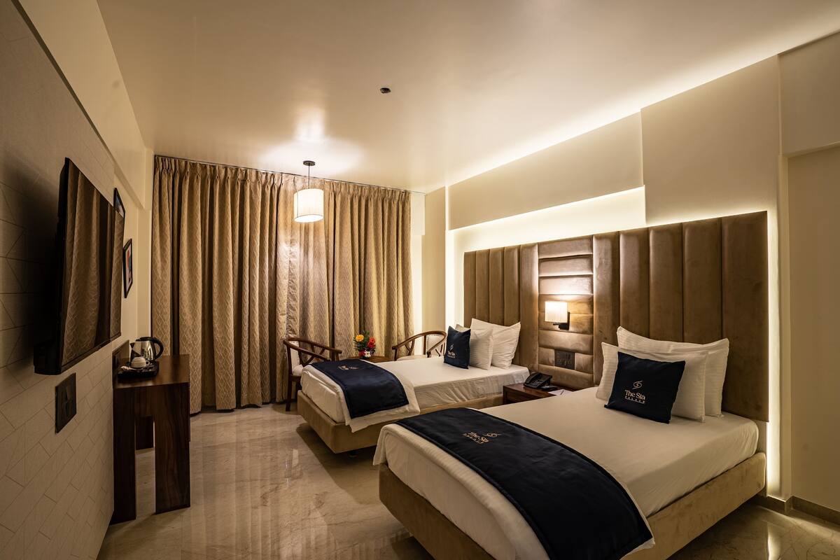 A hotel room with two beds, a desk, a chair, a TV, and a window with curtains.
