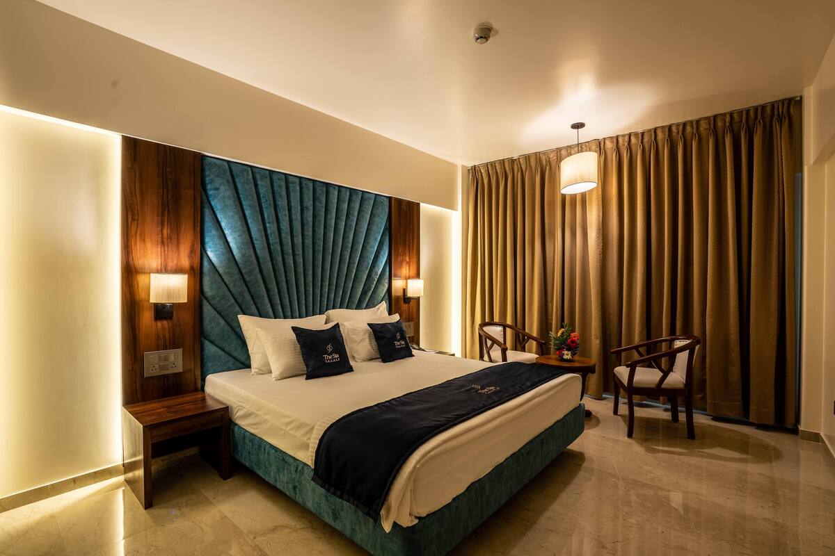 A hotel room with a large bed, a wooden headboard, a desk with a chair, and a large window with curtains.