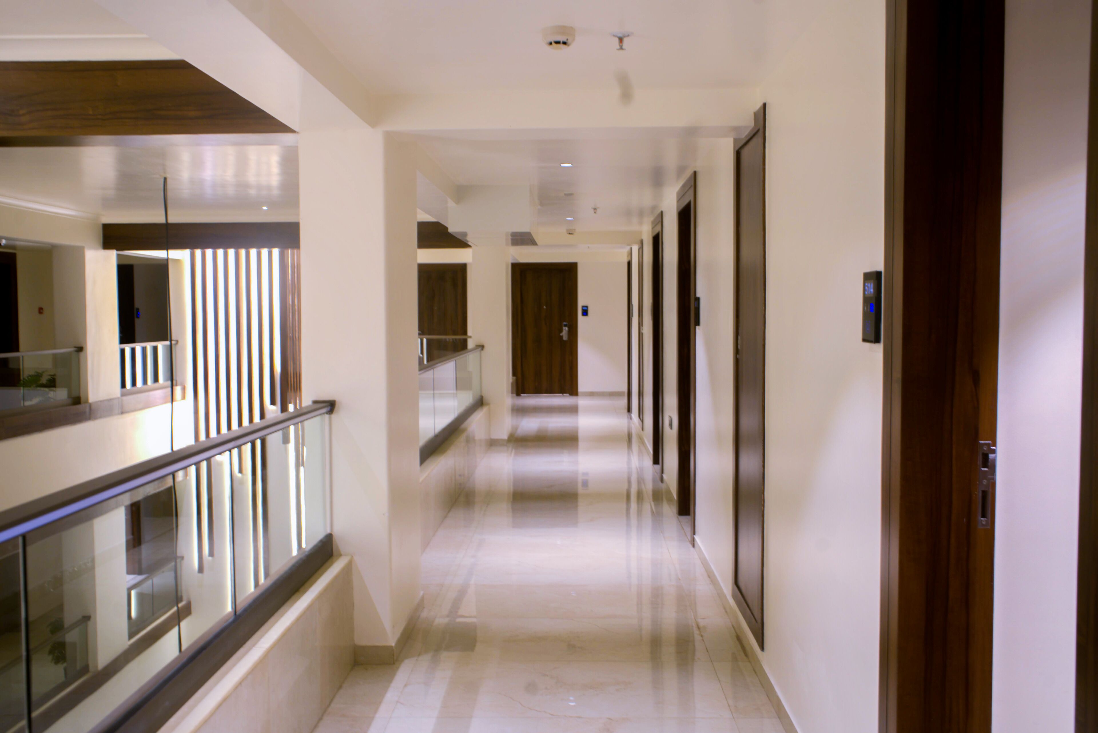 A hotel corridor with a glass railing, wooden doors, and a marble floor.