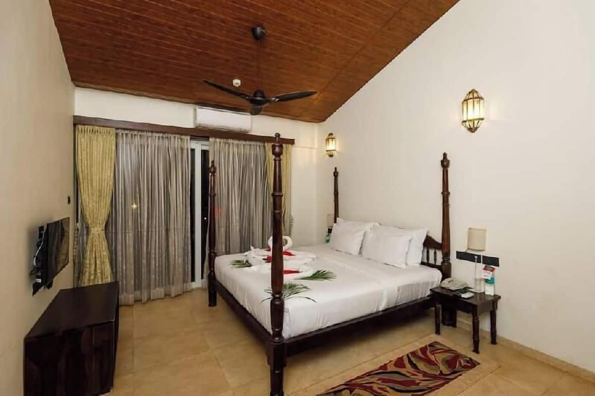A four-poster bed with white linens, a wooden ceiling fan, and two wall-mounted light fixtures.