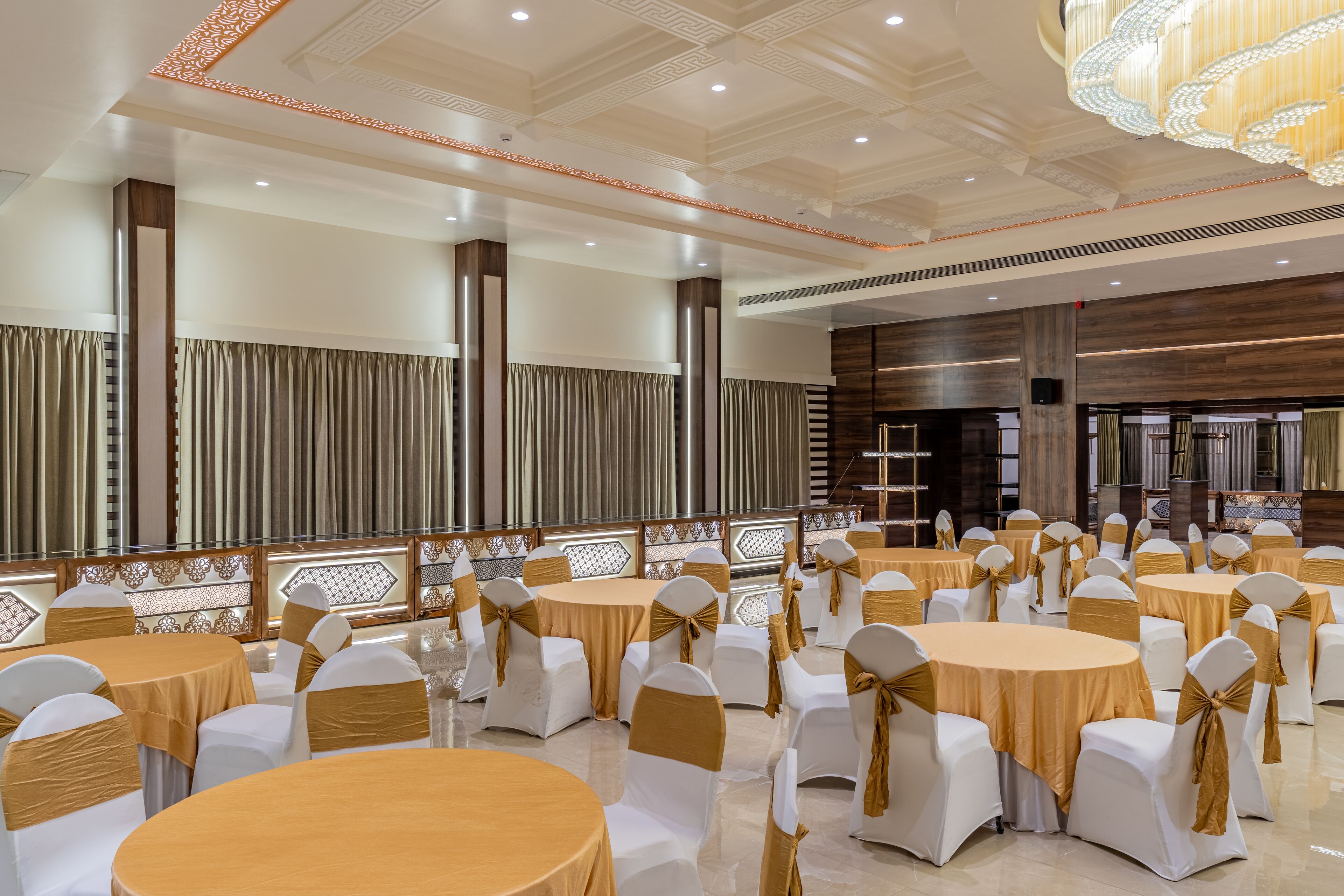 A banquet hall with round tables and white chairs, each with gold sashes.